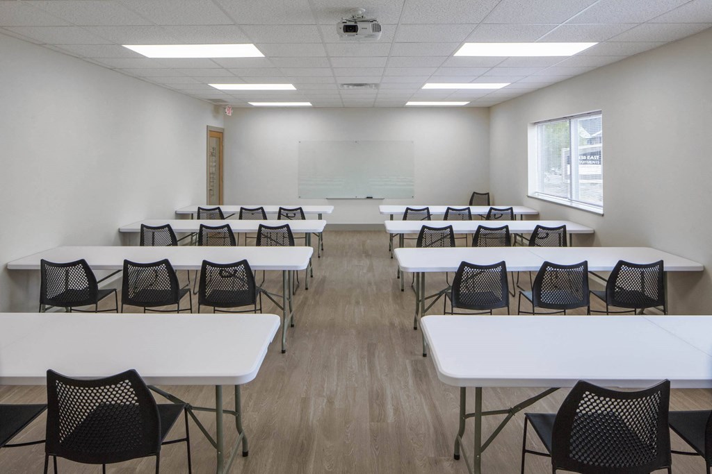 a classroom with white tables and chairs and a white projection screen