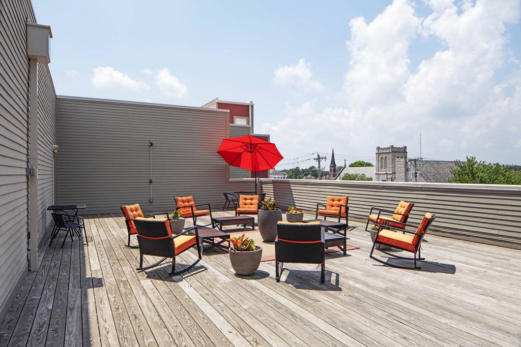 a rooftop patio with a red umbrella and chairs on a roof  at North Harrison Senior Apts, Shelbyville, IN, 46176