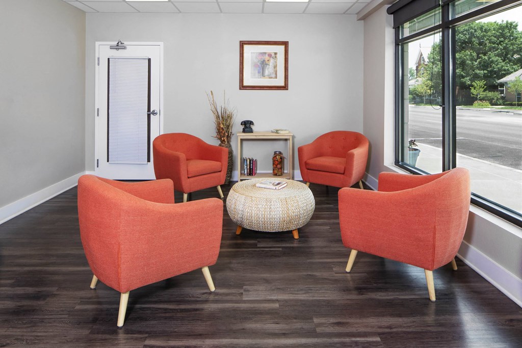 a living room with orange chairs and a table  and a window  a building with a sign on it in front of a bridge