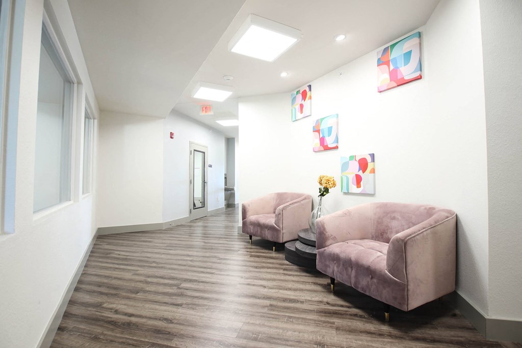 a long hallway with pink chairs and paintings on the wall at SouthPointe Village Apartments, LP, Fishers, 46038