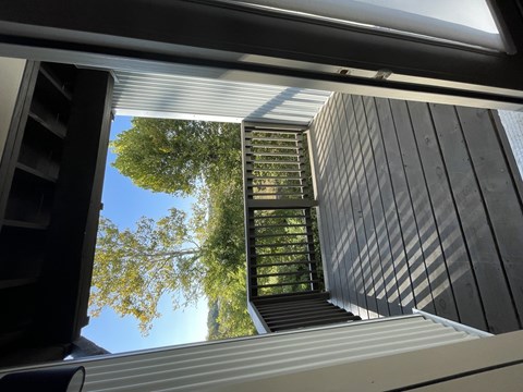 A view from inside a building looking up at a staircase leading to a balcony with trees in the background.