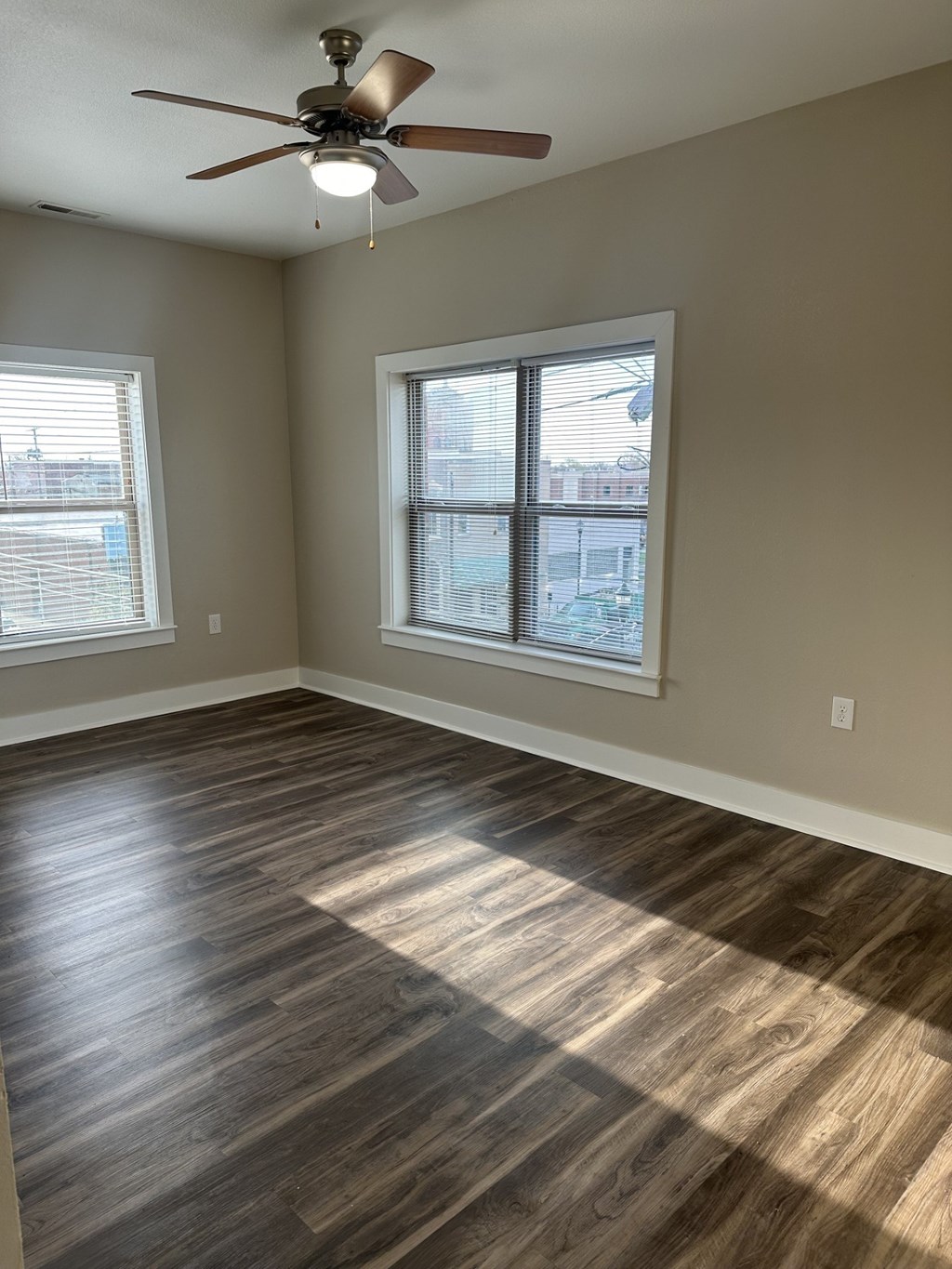 A room with a ceiling fan and two windows.
