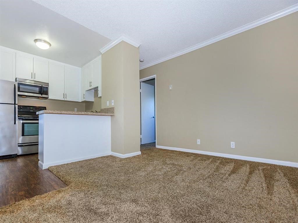 an empty living room and kitchen with a refrigerator and microwave