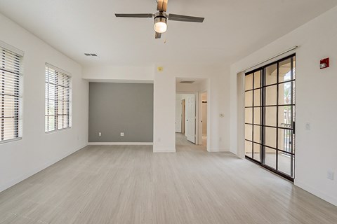an empty living room with a ceiling fan and a door to a hallway