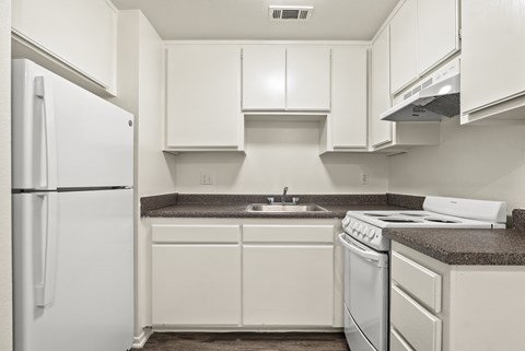 A white refrigerator is on the left in a kitchen with white cabinets and a white stove.