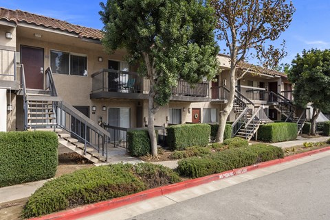 A row of apartment buildings with balconies and trees in front.