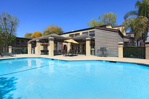 A large swimming pool in front of a house with a covered patio area.