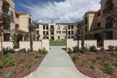 A concrete walkway leads through a landscaped courtyard between two rows of apartment buildings.