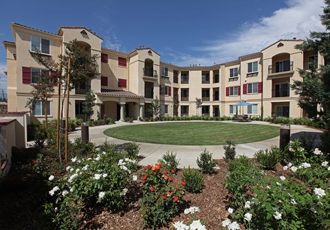 A large building with a courtyard surrounded by trees and flowers.