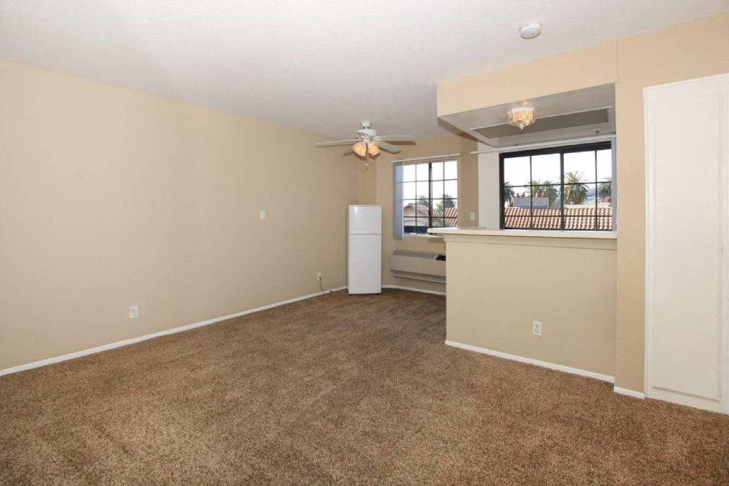 an empty living room with a kitchen and a ceiling fan