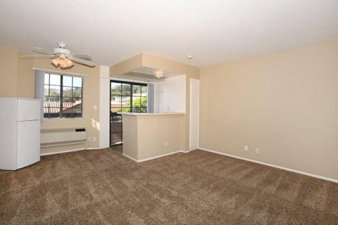 an empty living room with a kitchen and a ceiling fan