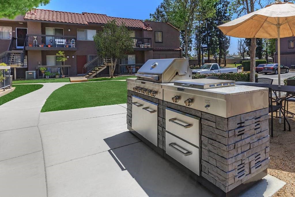 an outdoor grill with an umbrella on a sidewalk