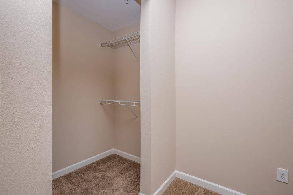 a walk in closet in an empty room with a mirrored wall