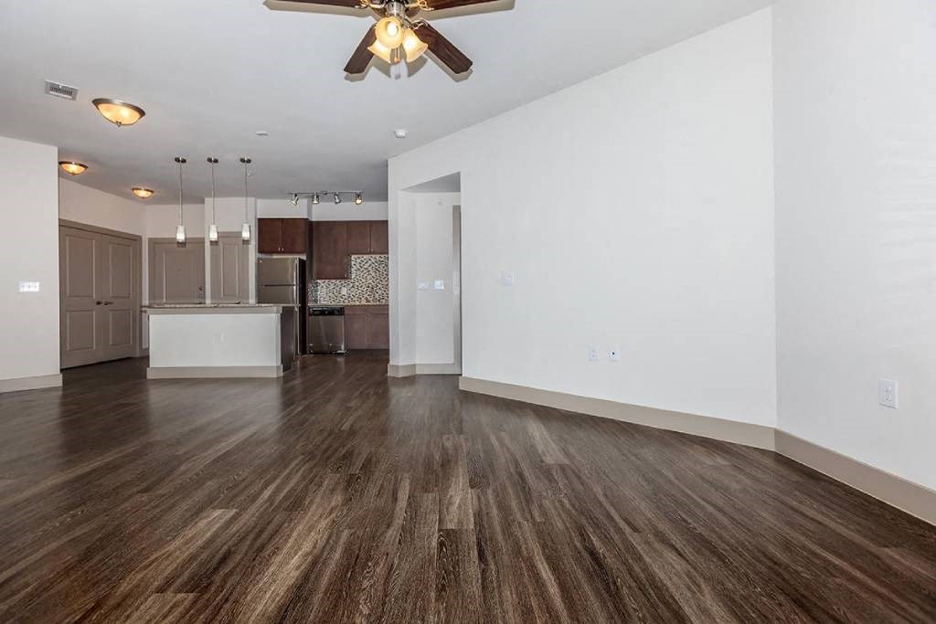an empty living room with a ceiling fan and a kitchen