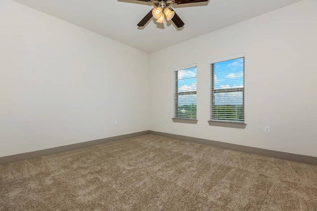 an empty room with a ceiling fan and two windows