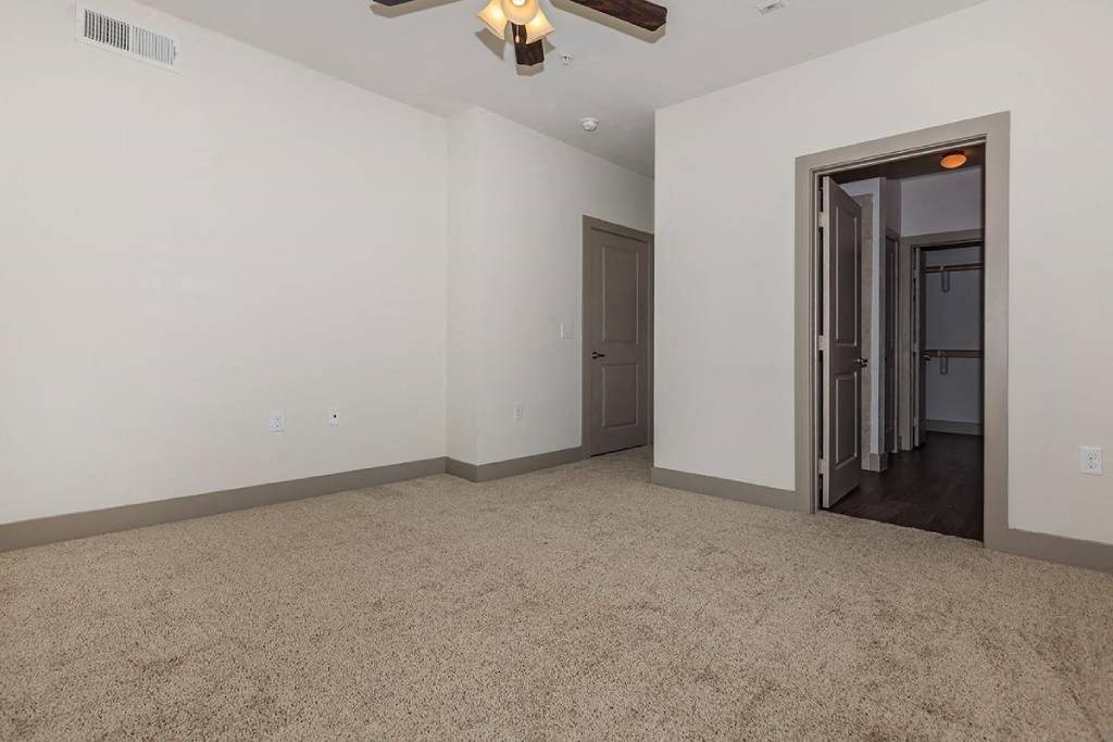an empty living room with a ceiling fan and a door to a hallway