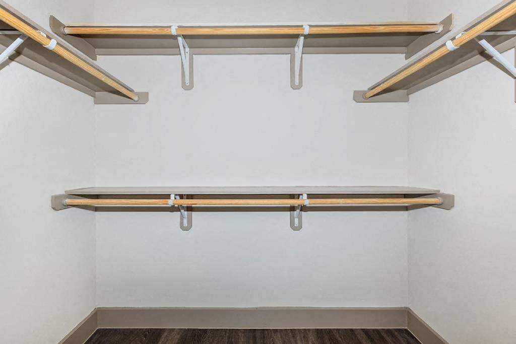 a walk in closet with a white wall and wooden shelves