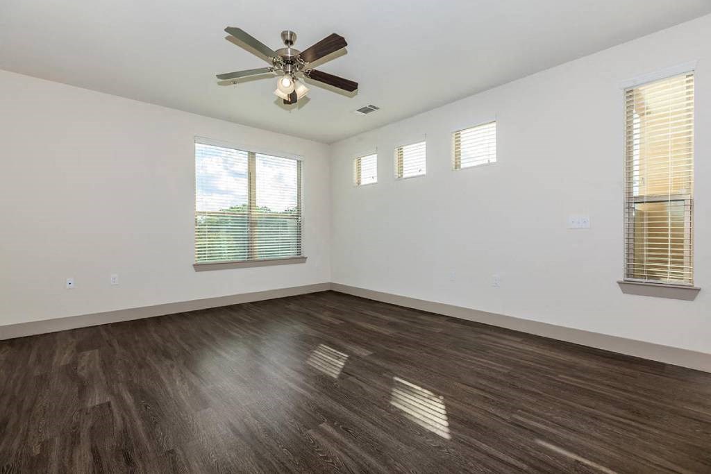 an empty living room with a ceiling fan and windows