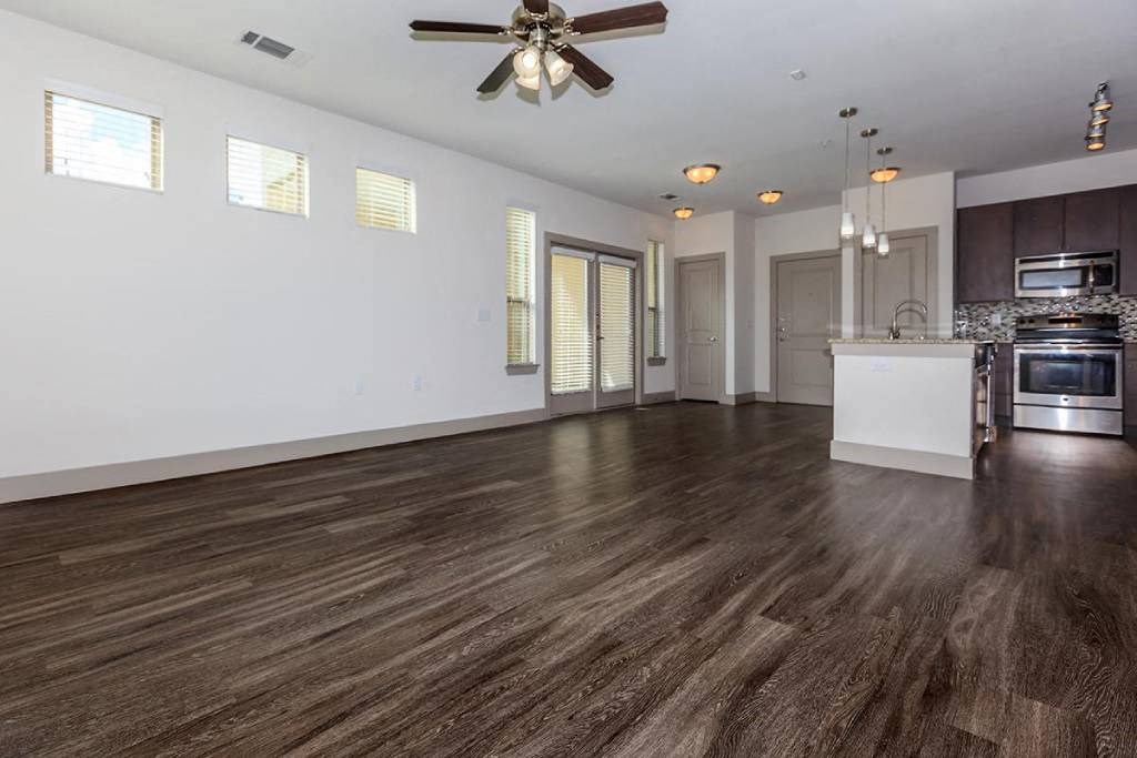 an empty living room with a kitchen and a ceiling fan