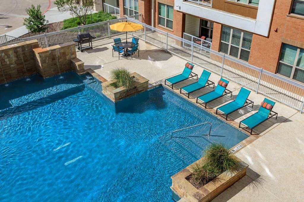 a large swimming pool with blue lounge chairs in front of a building