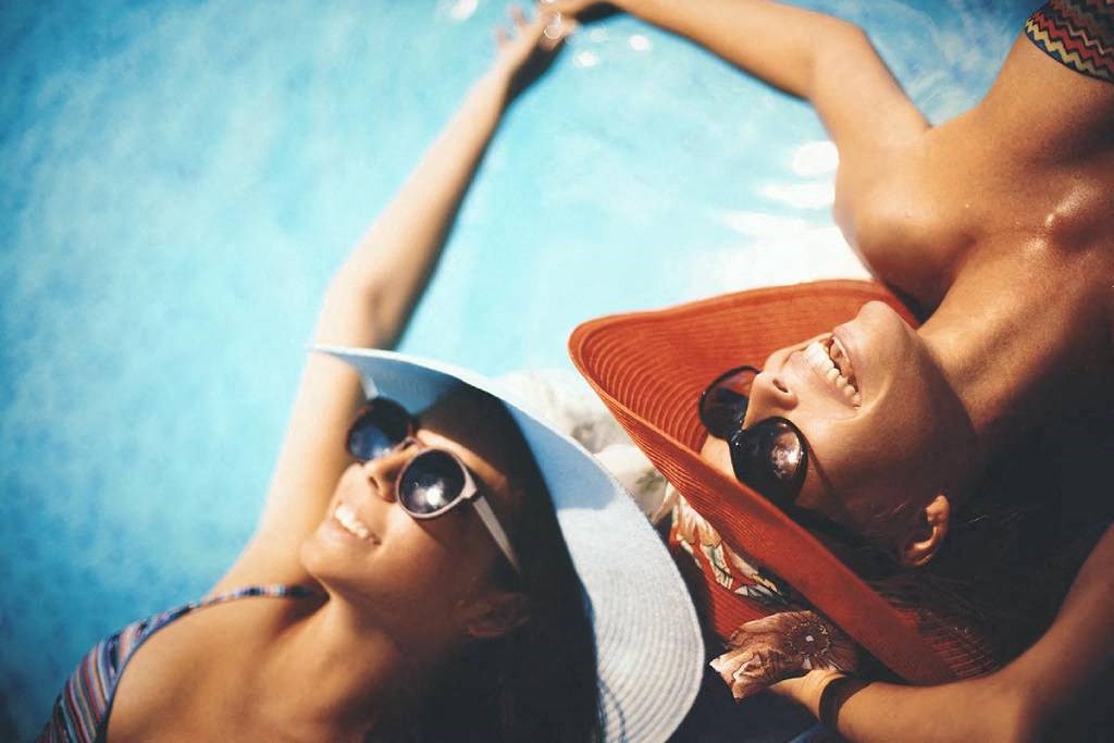two women laying on the beach wearing hats and sunglasses