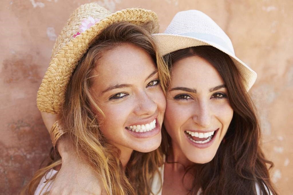 two women smiling while wearing hats and posing for a picture