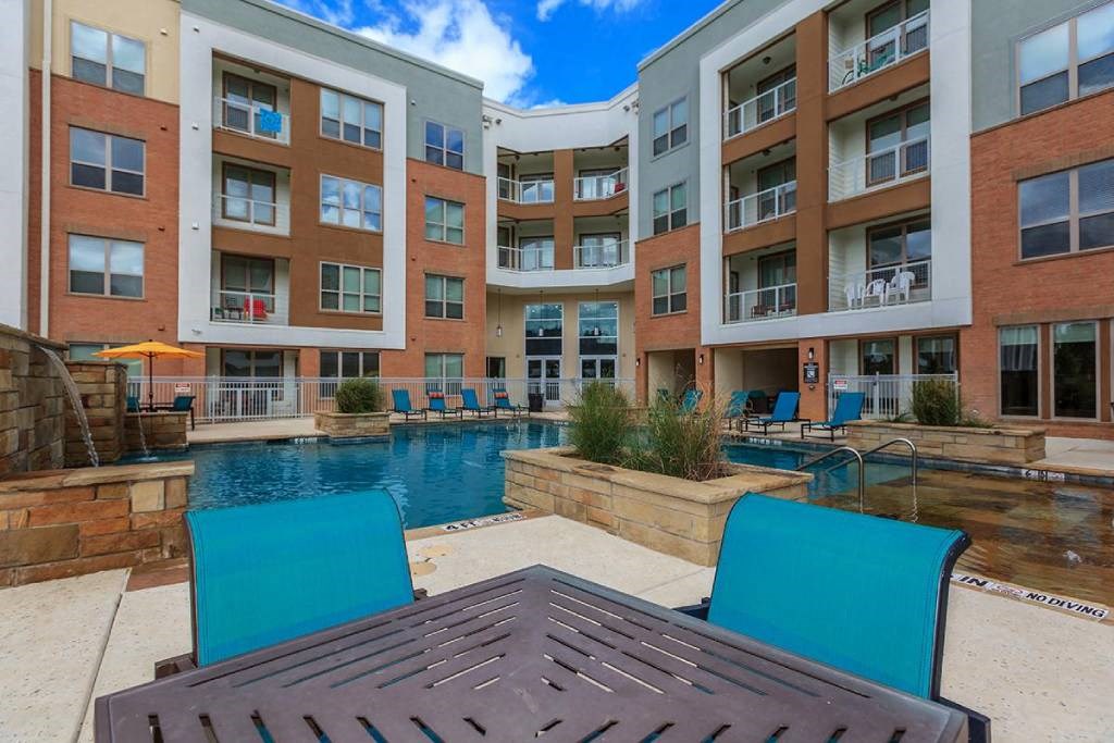 an outdoor pool with chairs and a table in front of an apartment building