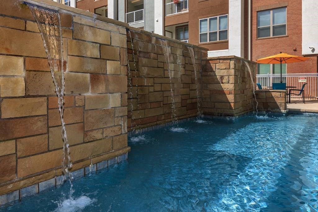 a swimming pool with a stone wall and waterfalls