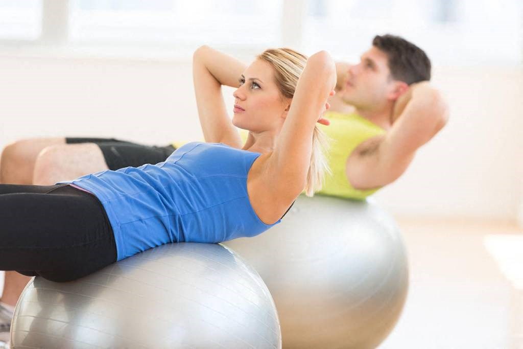 a man and woman doing exercises on exercise balls in a gym