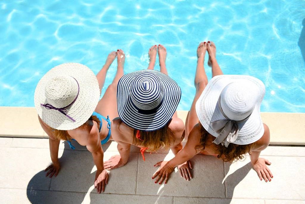 three women in hats sitting by a swimming pool