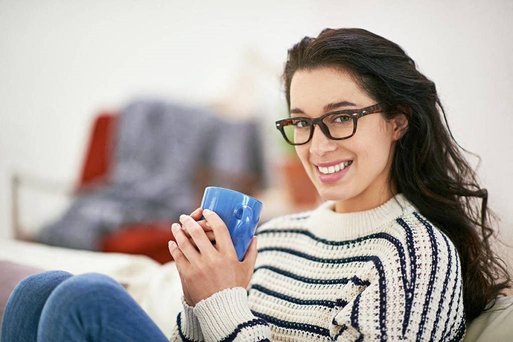 a woman sitting on a couch holding a blue coffee cup