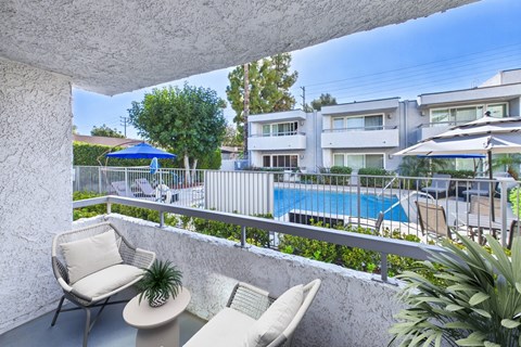 A balcony with a chair and a table overlooking a pool.