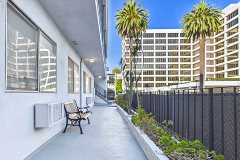 A long concrete walkway with a bench and a fence on the right side.
