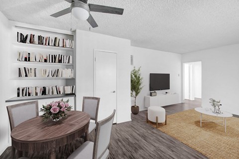 A living room with a round wooden table and chairs, a television, a bookshelf, and a rug.