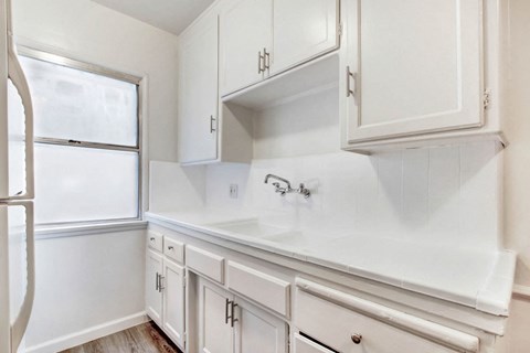 A white kitchen with a refrigerator, cabinets, and a counter.