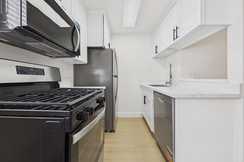 A black stove top oven sits in a kitchen with white cabinets and a black refrigerator.