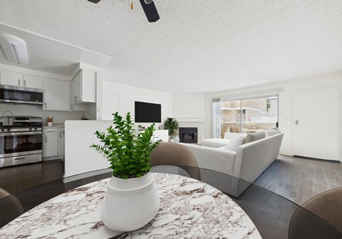 A plant in a white pot sits on a marble table in a modern kitchen and living room.