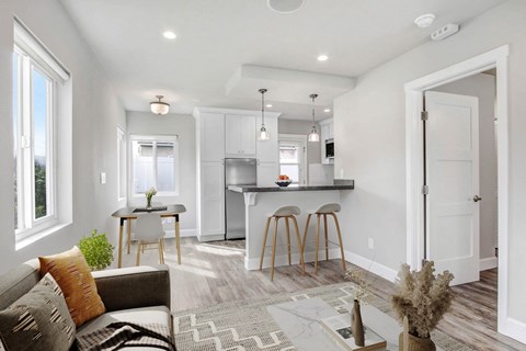 A modern living room with a grey sofa and a kitchen area in the background.