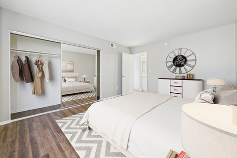 A bedroom with a large bed and a wardrobe with clothes hanging.