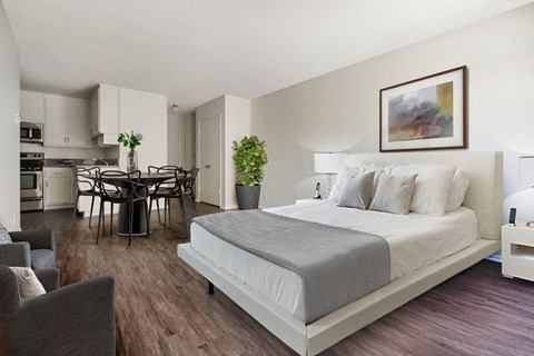 A bedroom with a large bed and a dining area in the background.