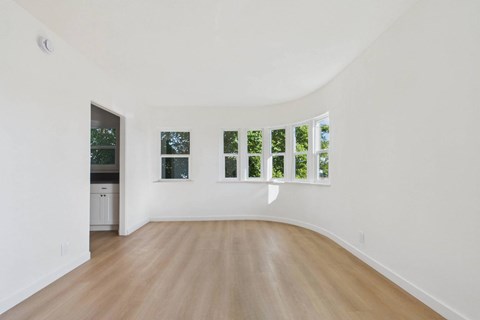 A white room with a wooden floor and a window with a view of trees.
