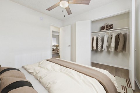 A bedroom with a bed and a closet with clothes hanging.