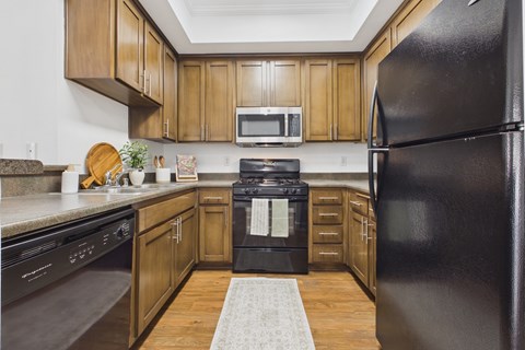 A black refrigerator stands in a kitchen with wooden cabinets and a black oven.