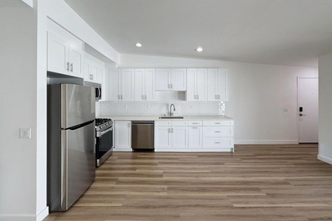 A modern kitchen with white cabinets and a wooden floor.