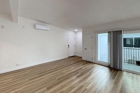 A room with wooden flooring and a sliding glass door leading to a balcony.