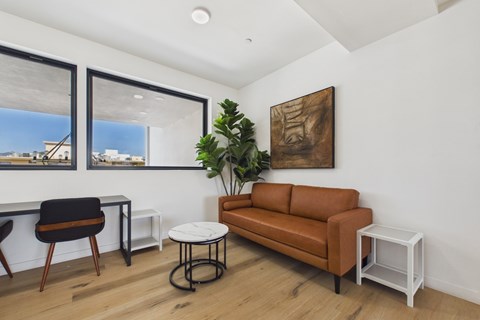 A living room with a brown couch, a black chair, a white table, and a painting on the wall.