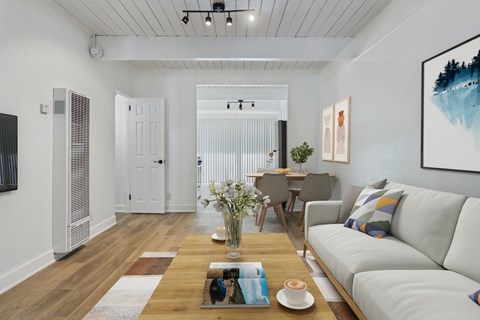 A modern living room with a white sofa, a wooden coffee table, and a painting on the wall.