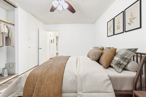 A bedroom with a bed covered in a white comforter and a brown throw.