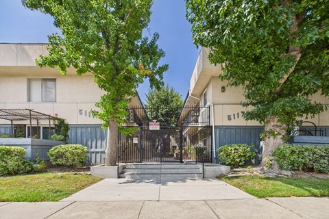 A white building with a black gate and a tree in front.