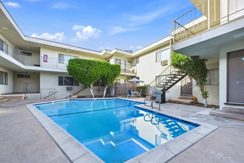 A swimming pool in front of a building with a blue sky and clouds in the background.